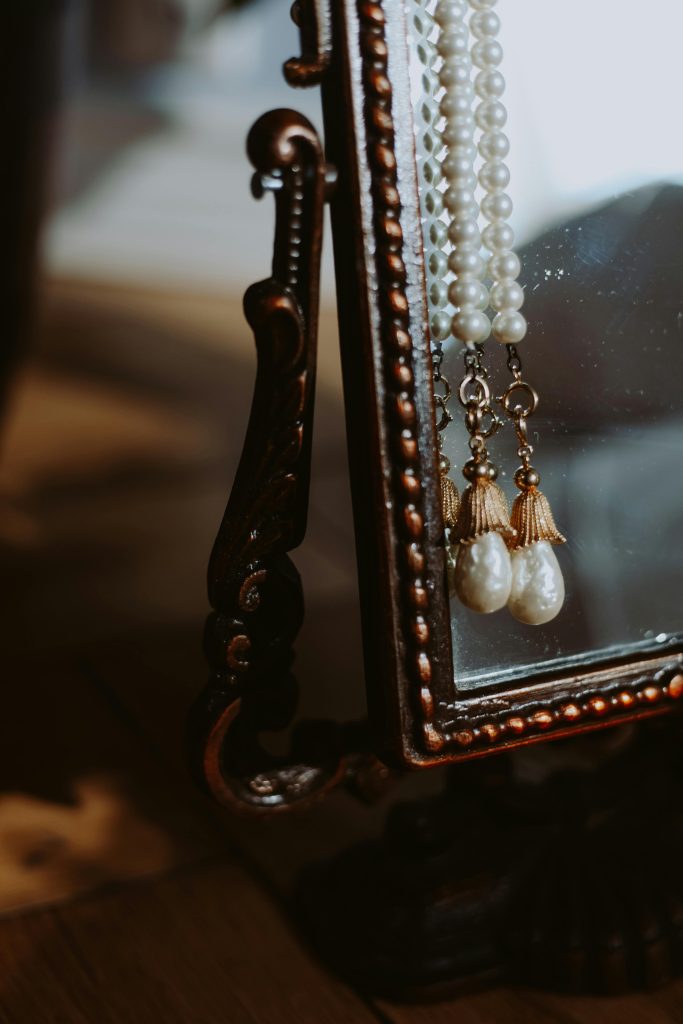 Close-up of luxurious vintage pearl jewelry hanging on an ornate mirror.