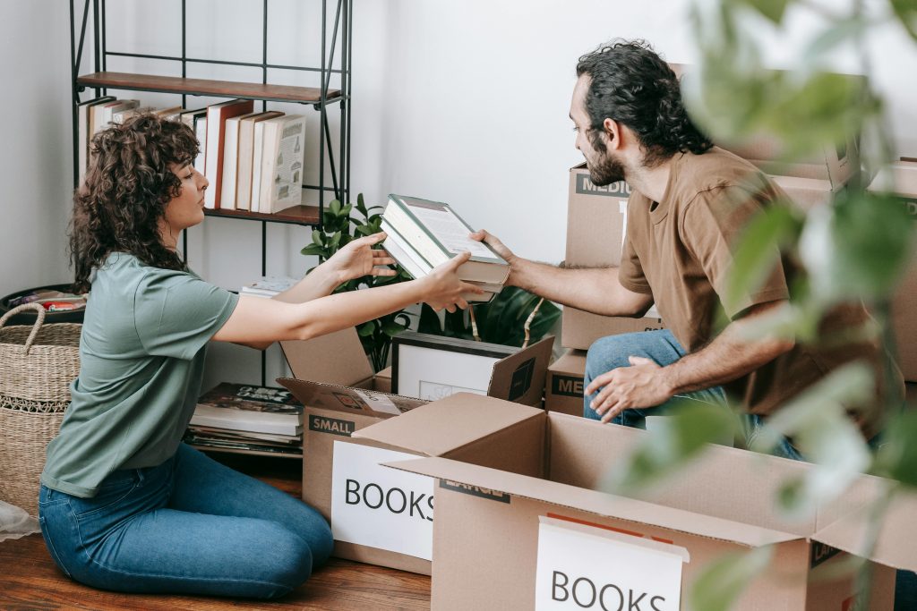 A couple organizing and packing books in cardboard boxes indoors, preparing for a move.